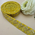 Roll of yellow lace ribbon with floral patterns next to a white flower on a light background