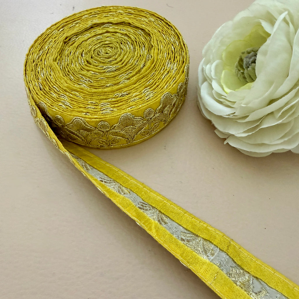 Roll of yellow ribbon with floral pattern next to a white flower on a beige background