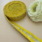 Roll of yellow ribbon with floral pattern next to a white flower on a beige background