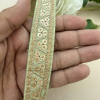 Decorative gold ribbon held between fingers with a blurred floral background