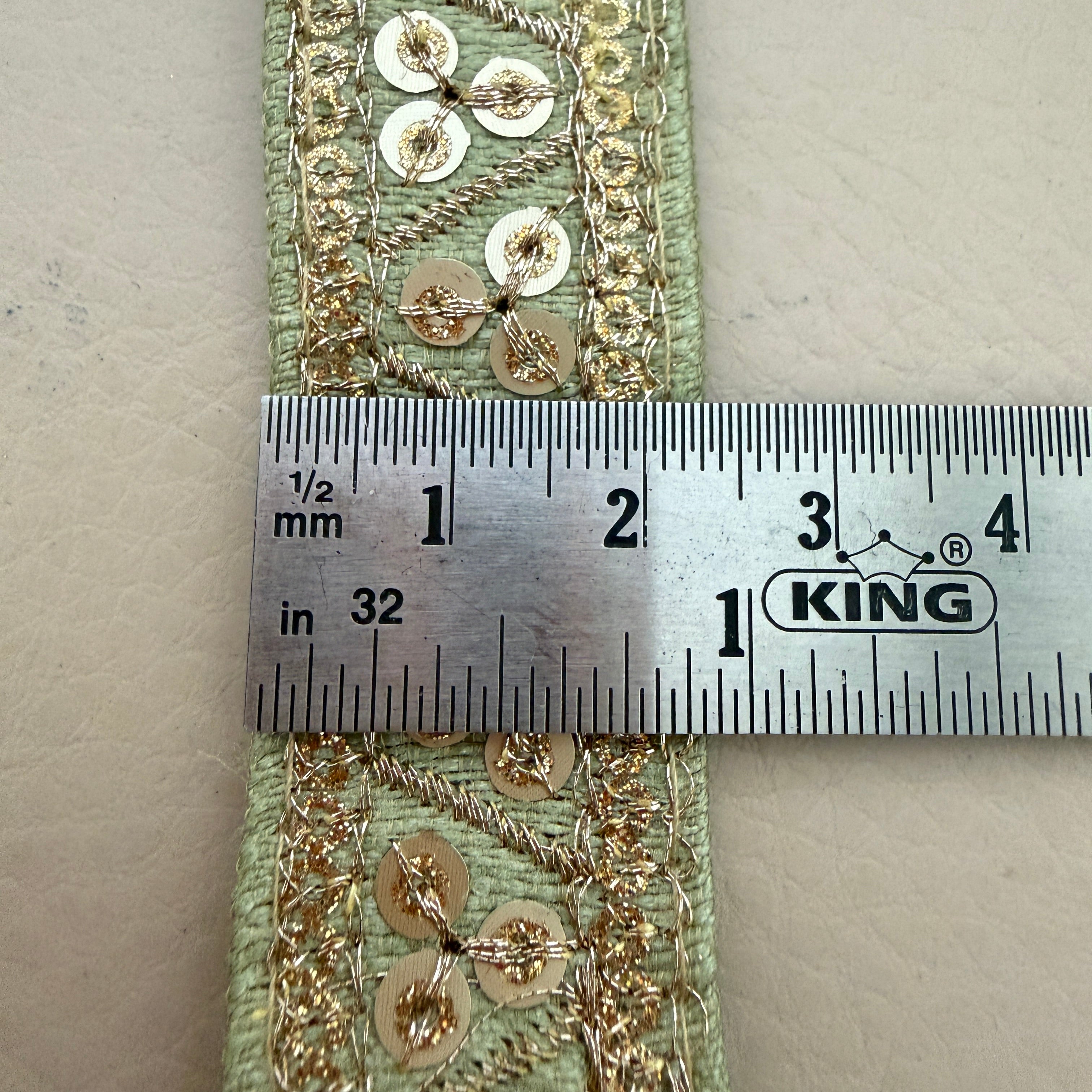Decorative ribbon with gold embellishments measured against a ruler on a beige background