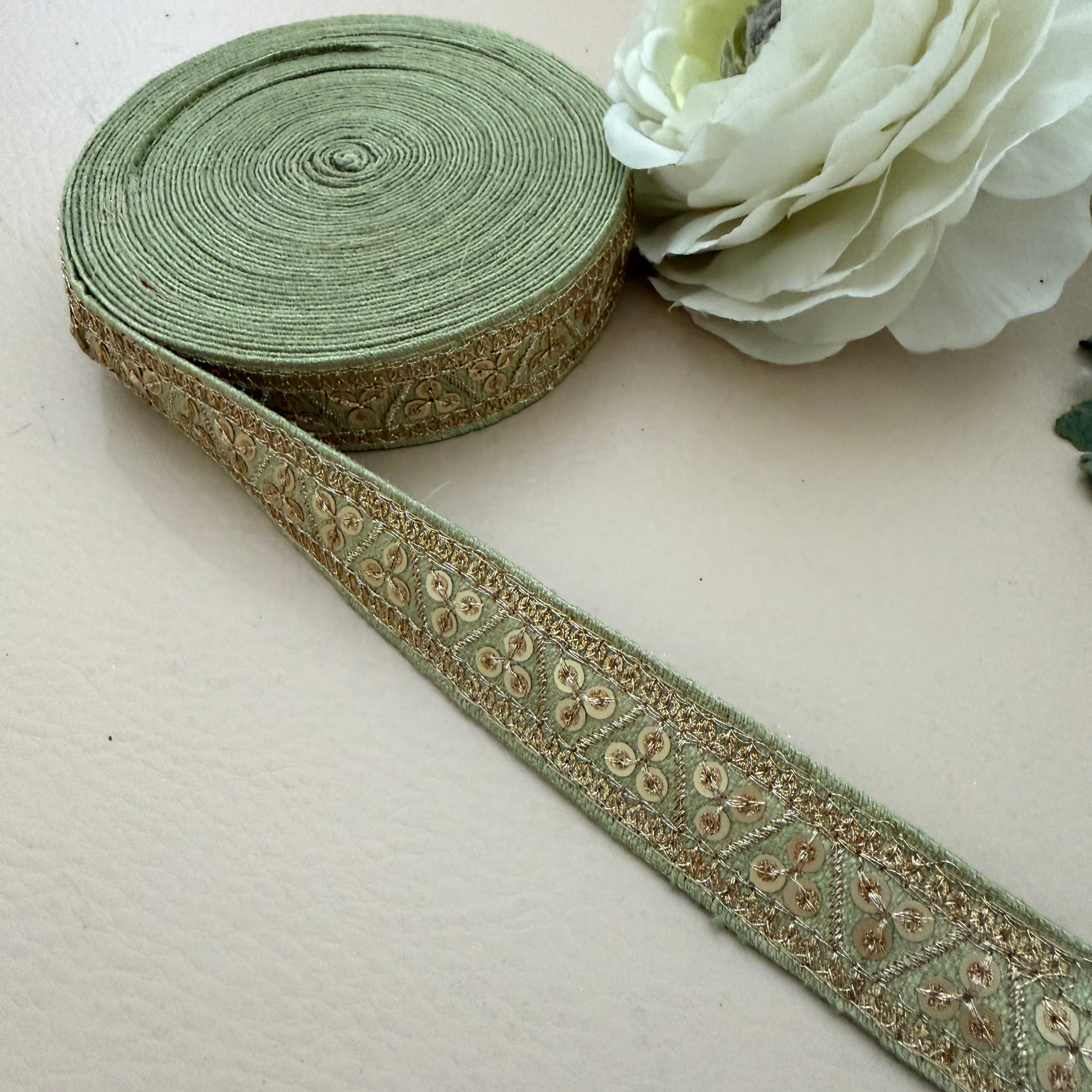 Green ribbon with decorative pattern on a light surface next to a white flower.