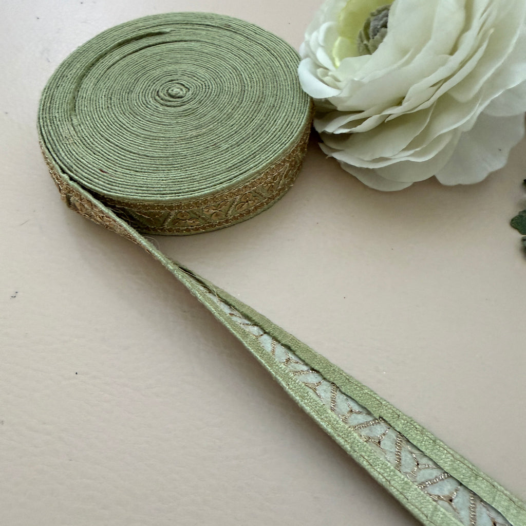 Green ribbon with decorative pattern on a beige surface next to a white flower.