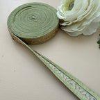 Green ribbon with decorative pattern on a beige surface next to a white flower.