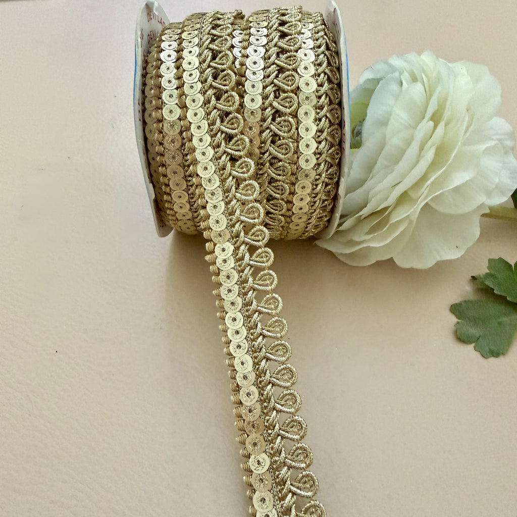 Gold sequin ribbon spool with a white flower on a beige background