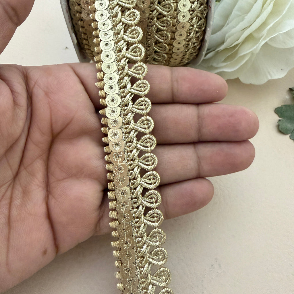 Gold lace trim held between fingers with a neutral background