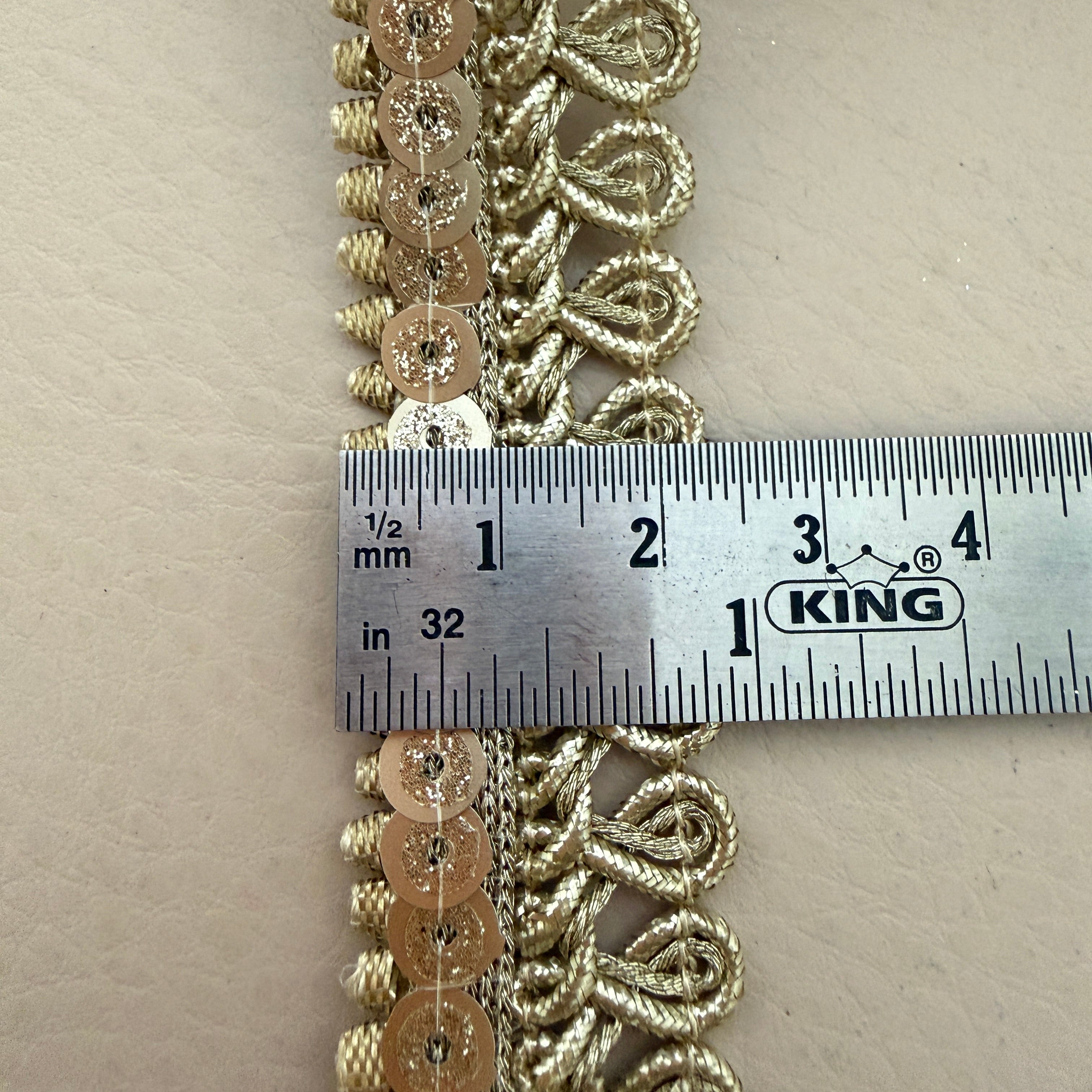 Decorative gold lace strip with a ruler for scale on a beige background