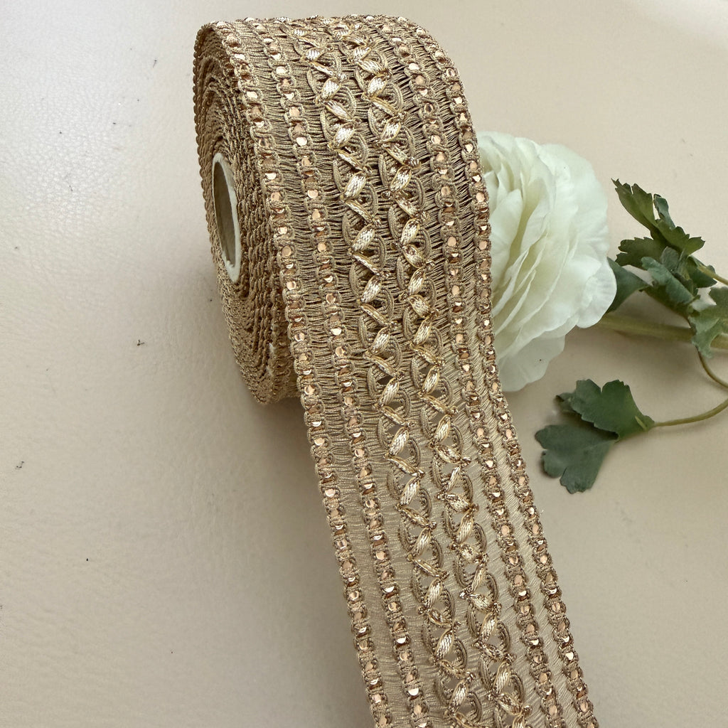 Roll of decorative gold ribbon with a white flower on a beige background