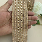 Gold lace trim held by a hand with a white flower in the background