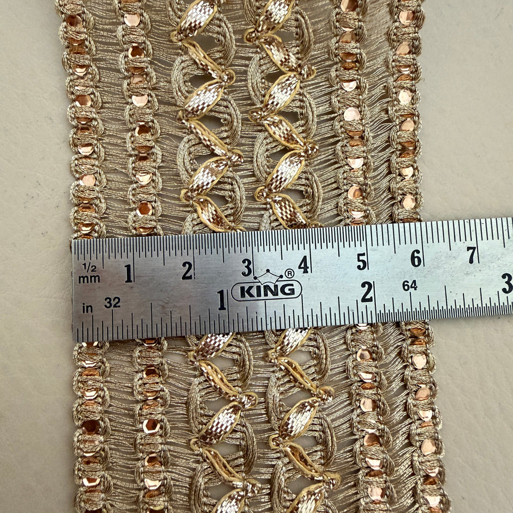 Decorative fabric trim with gold embroidery and a ruler for scale on a neutral background