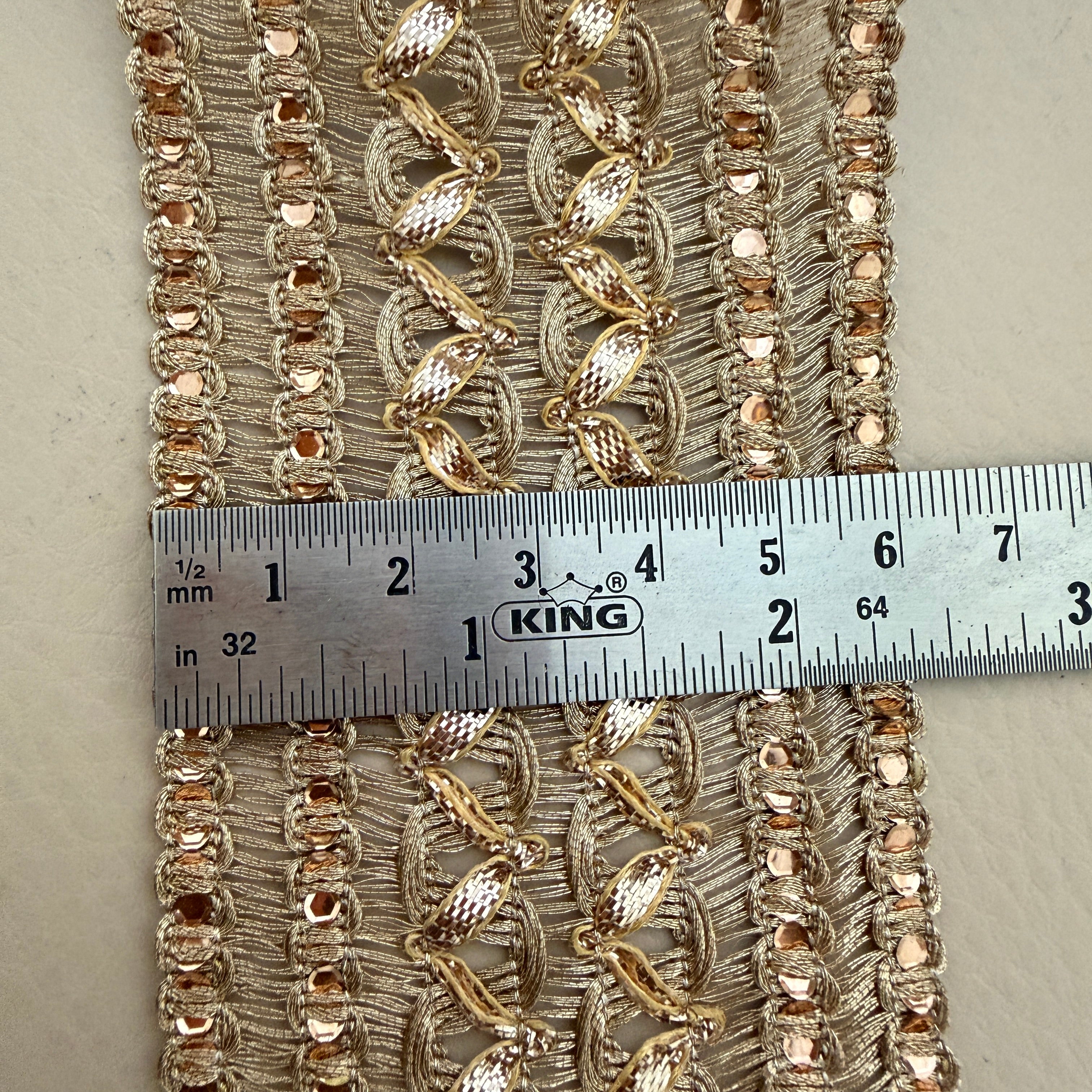 Decorative fabric trim with gold embroidery and a ruler for scale on a neutral background