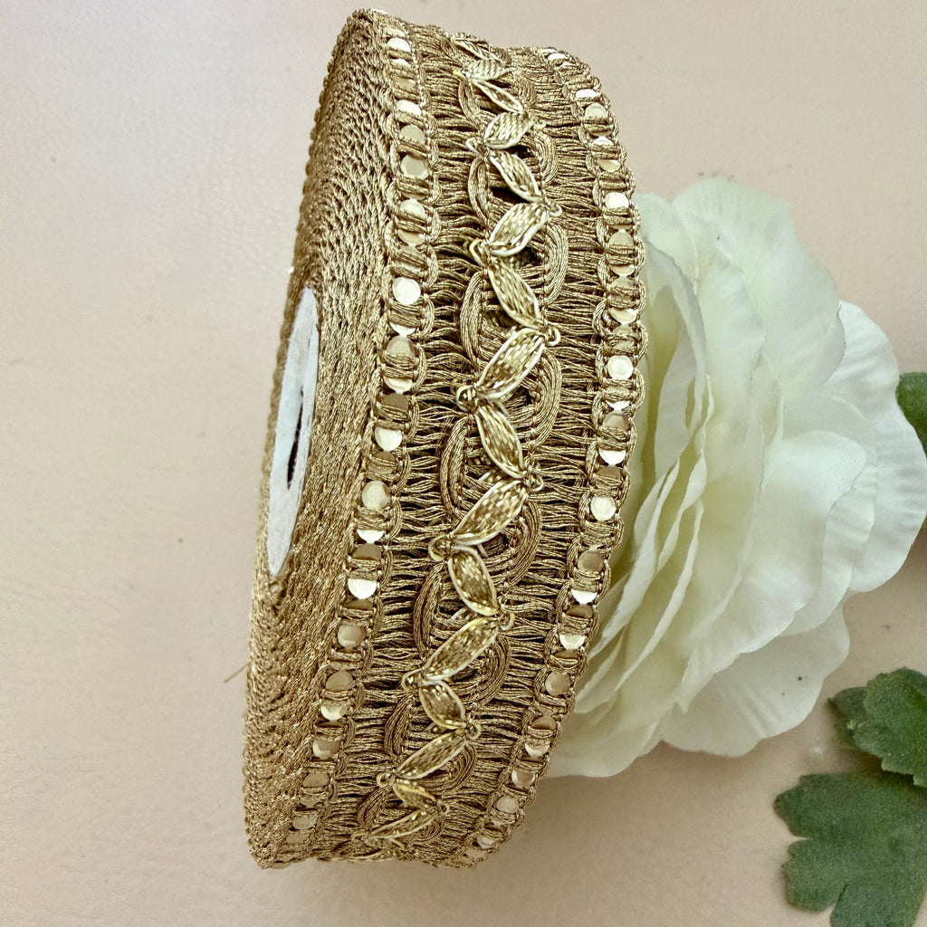 Decorative gold ribbon with intricate patterns next to a white flower on a beige background