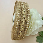 Decorative gold ribbon with intricate patterns next to a white flower on a beige background
