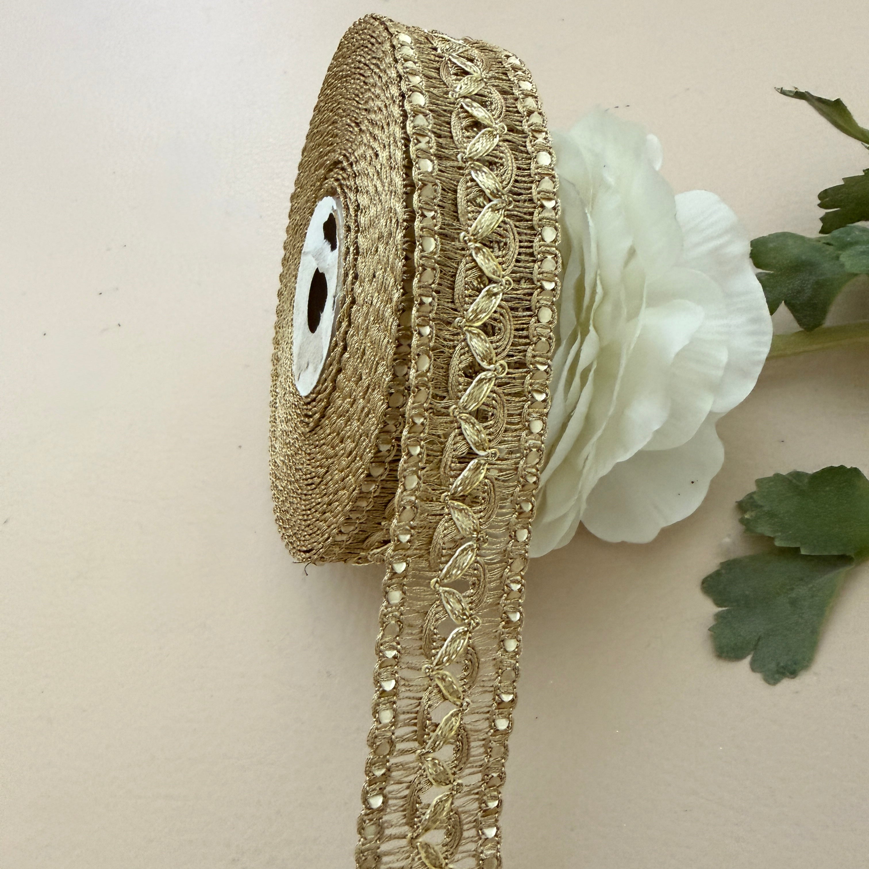 Decorative gold ribbon with beads and a white flower on a beige background