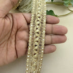Gold lace trim held between fingers with a neutral background