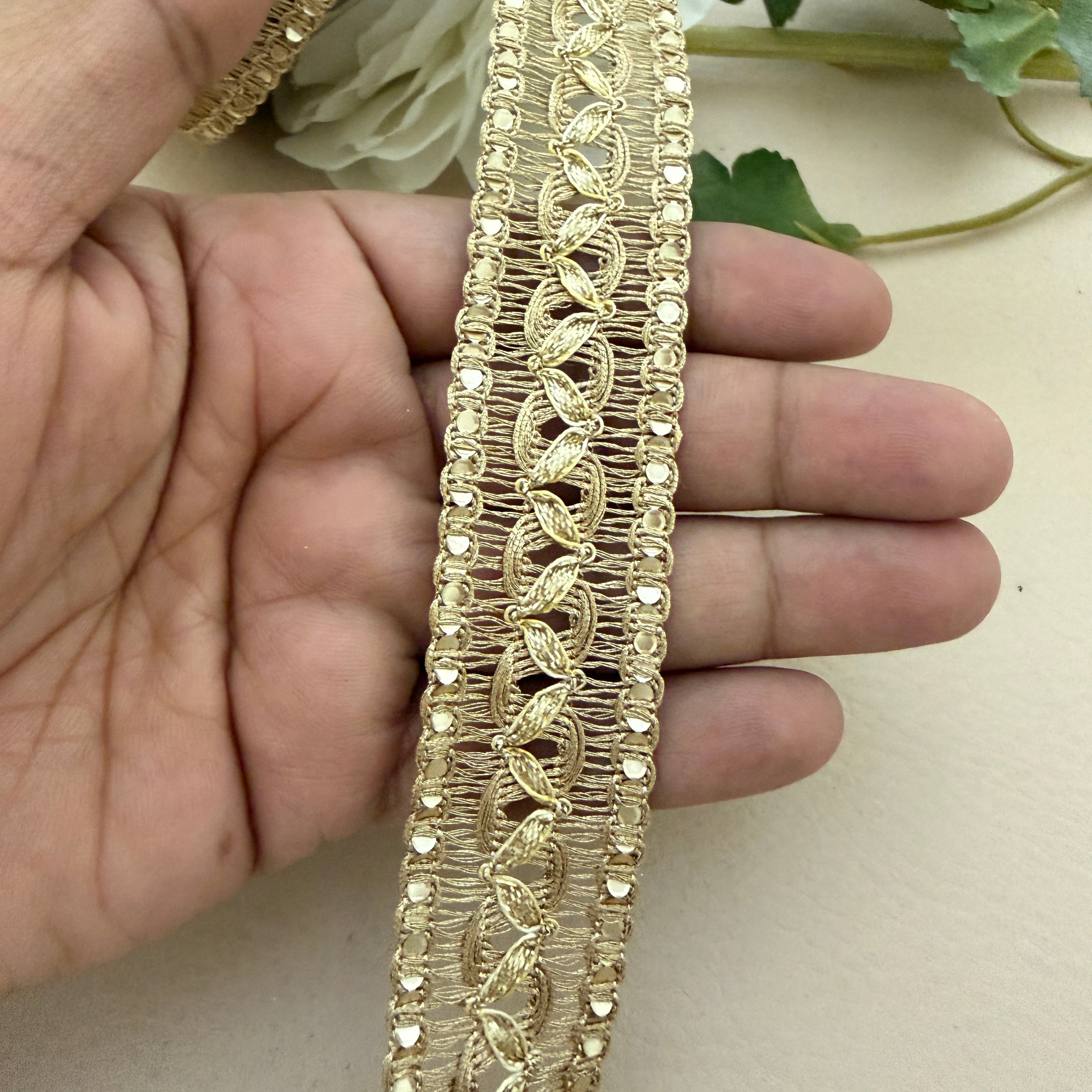 Gold lace trim held between fingers with a neutral background