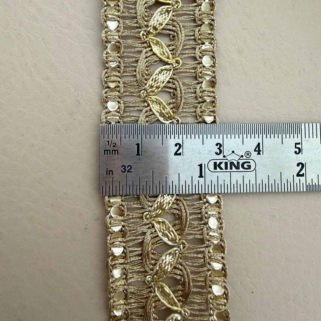 Decorative gold lace fabric with a ruler for scale on a neutral background