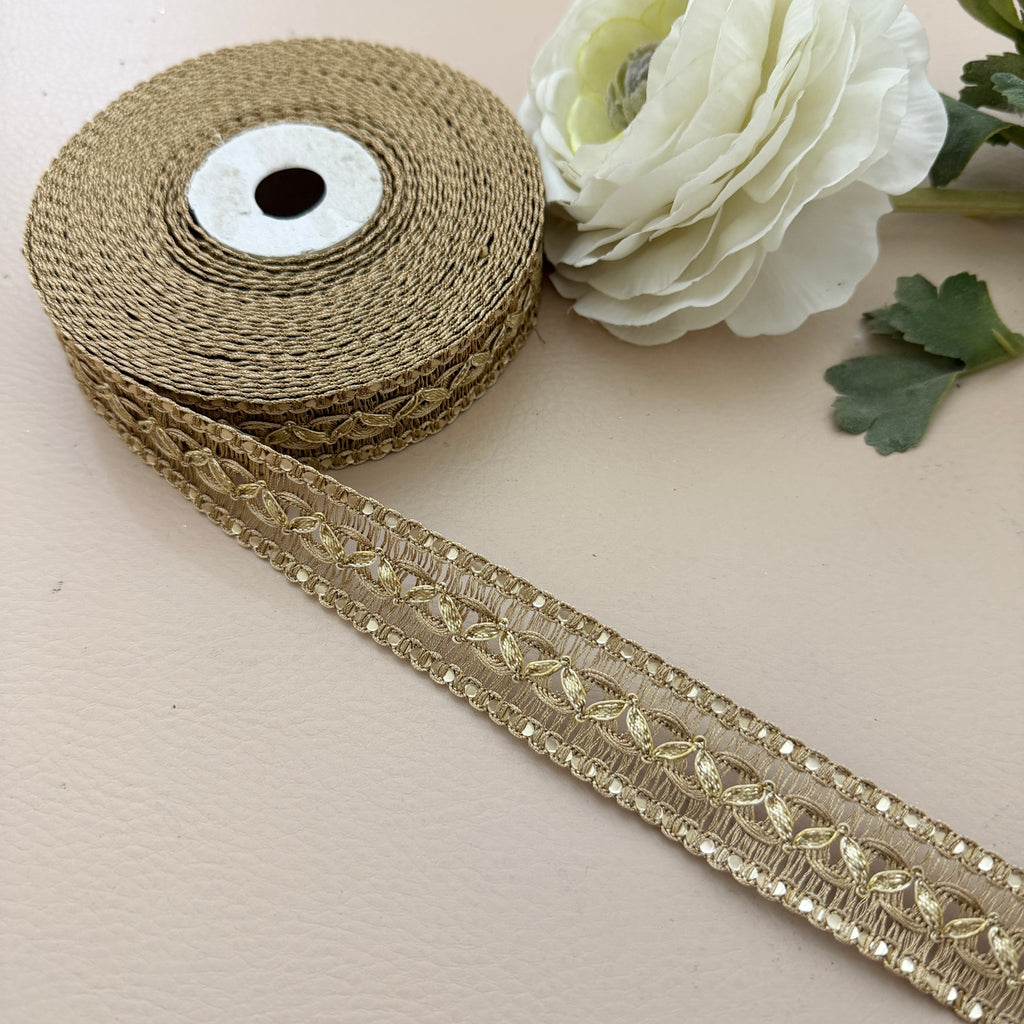 Roll of gold lace ribbon with a white flower on a beige background