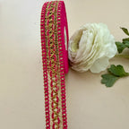 Decorative ribbon with gold and pink pattern next to a white flower on a beige background