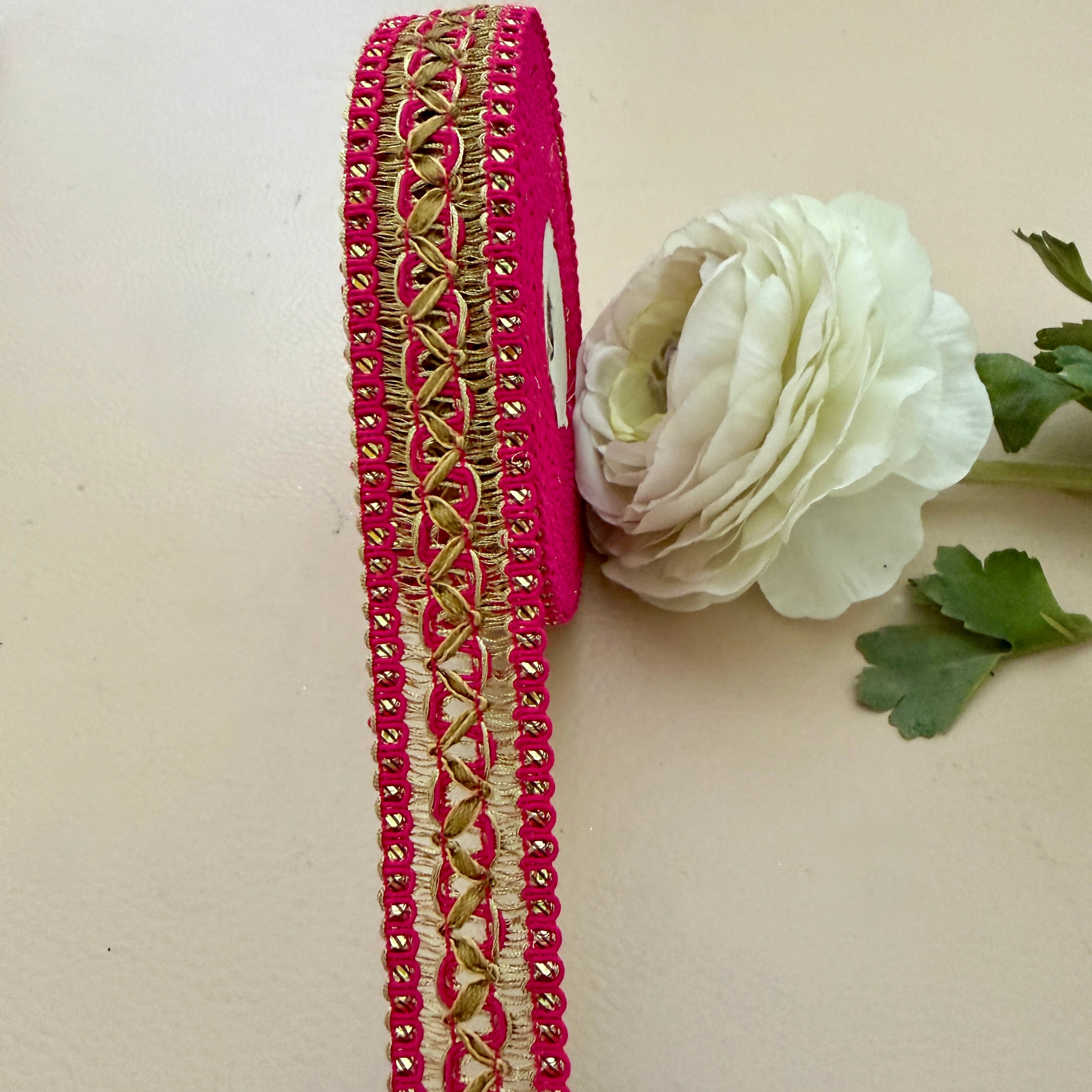 Decorative ribbon with gold and pink pattern next to a white flower on a beige background