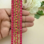 Decorative pink and gold trim held between fingers with a white flower in the background