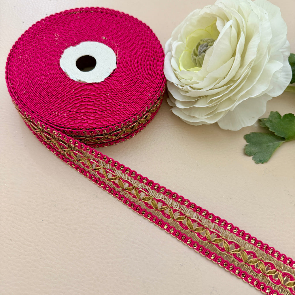 Roll of pink ribbon with gold lace trim next to a white flower on a beige background