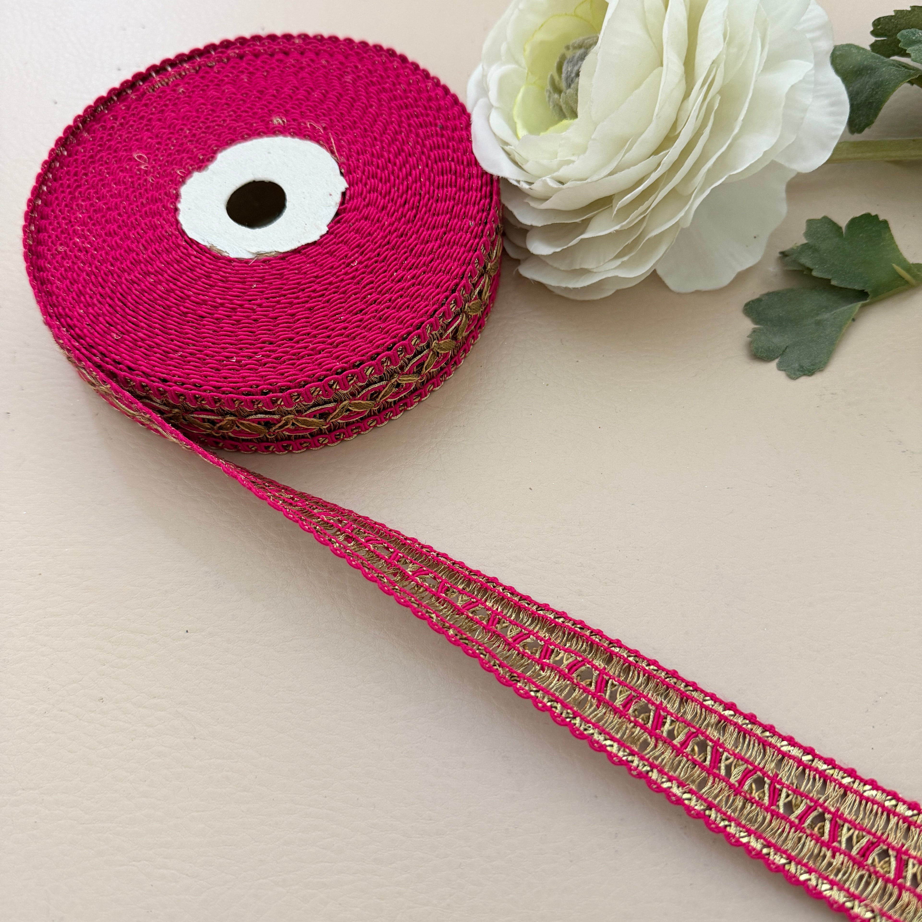 Pink ribbon with gold edge on a beige surface with a white flower.
