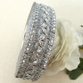 Silver decorative ribbon with intricate patterns on a beige background with a white flower.