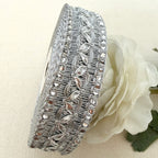 Silver decorative ribbon with intricate patterns on a beige background with a white flower.