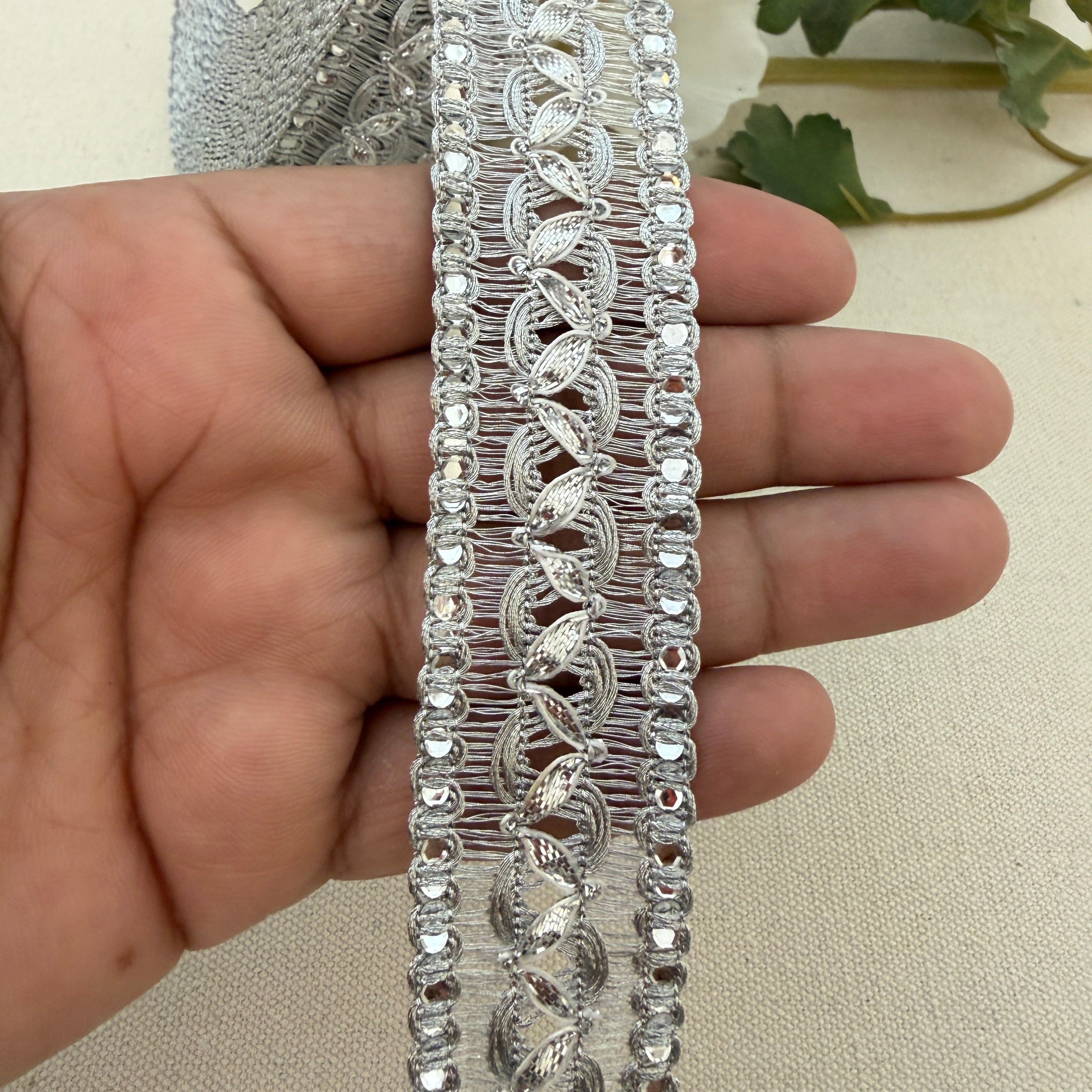 Decorative silver lace trim held by a hand against a neutral background