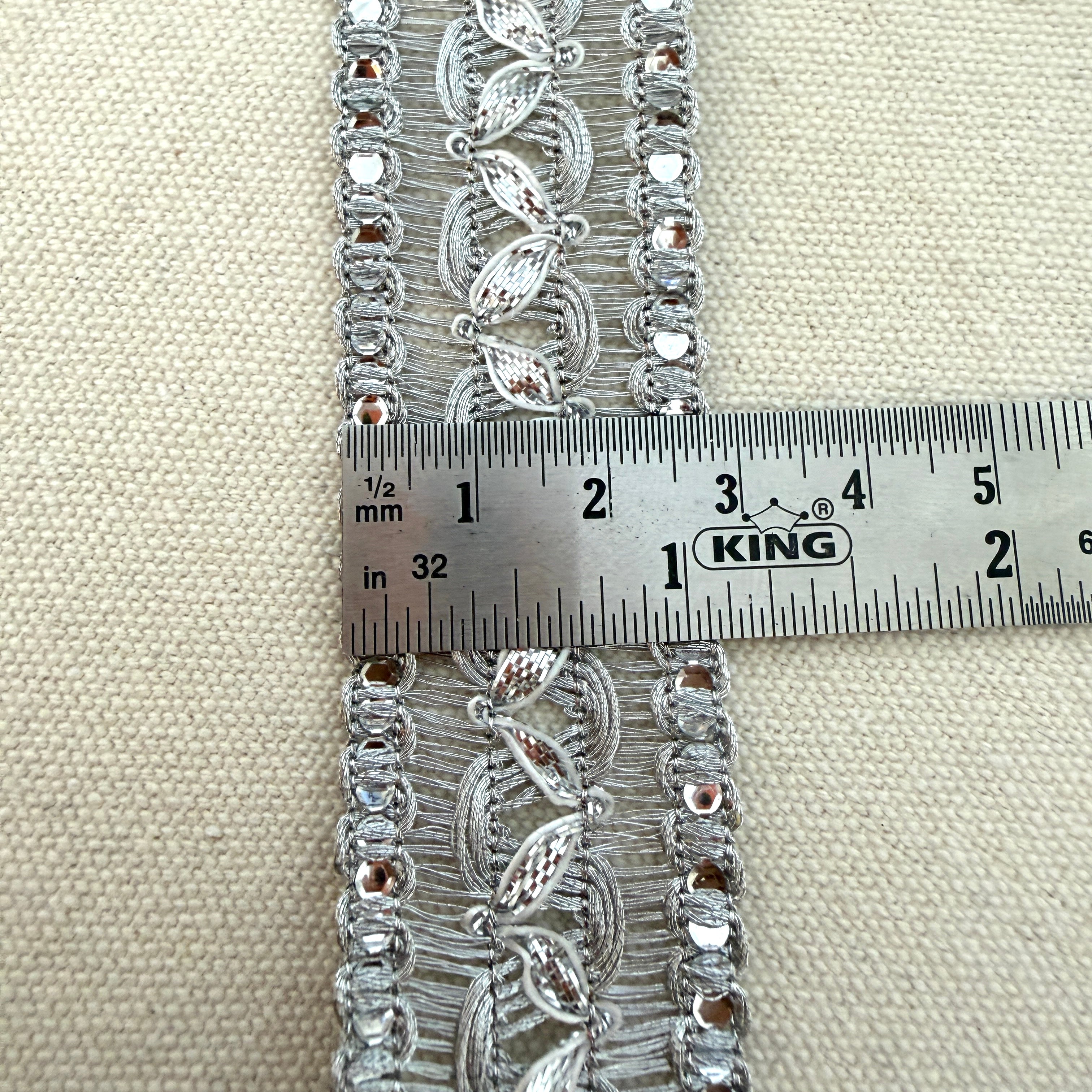 Decorative lace trim with a ruler for scale on a beige fabric background