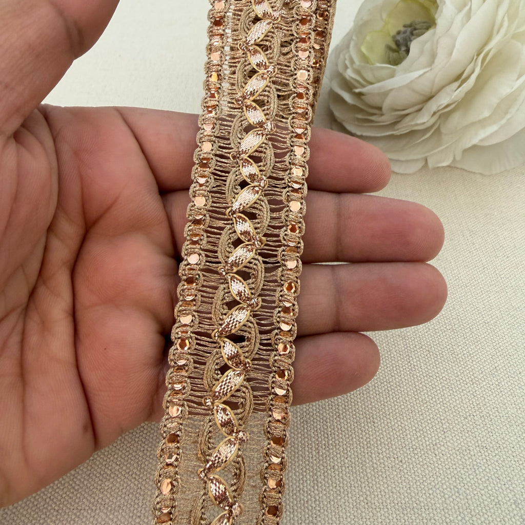 Rose gold lace trim held between fingers with a white flower in the background