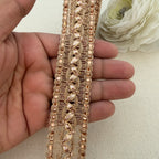 Rose gold lace trim held between fingers with a white flower in the background