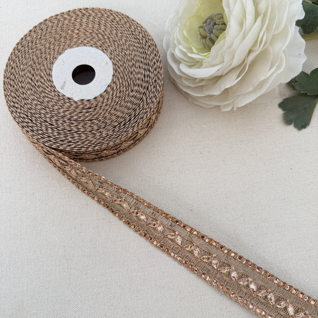 Spool of brown ribbon with decorative trim on a light background with a white flower.