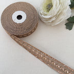 Spool of brown ribbon with decorative trim on a light background with a white flower.