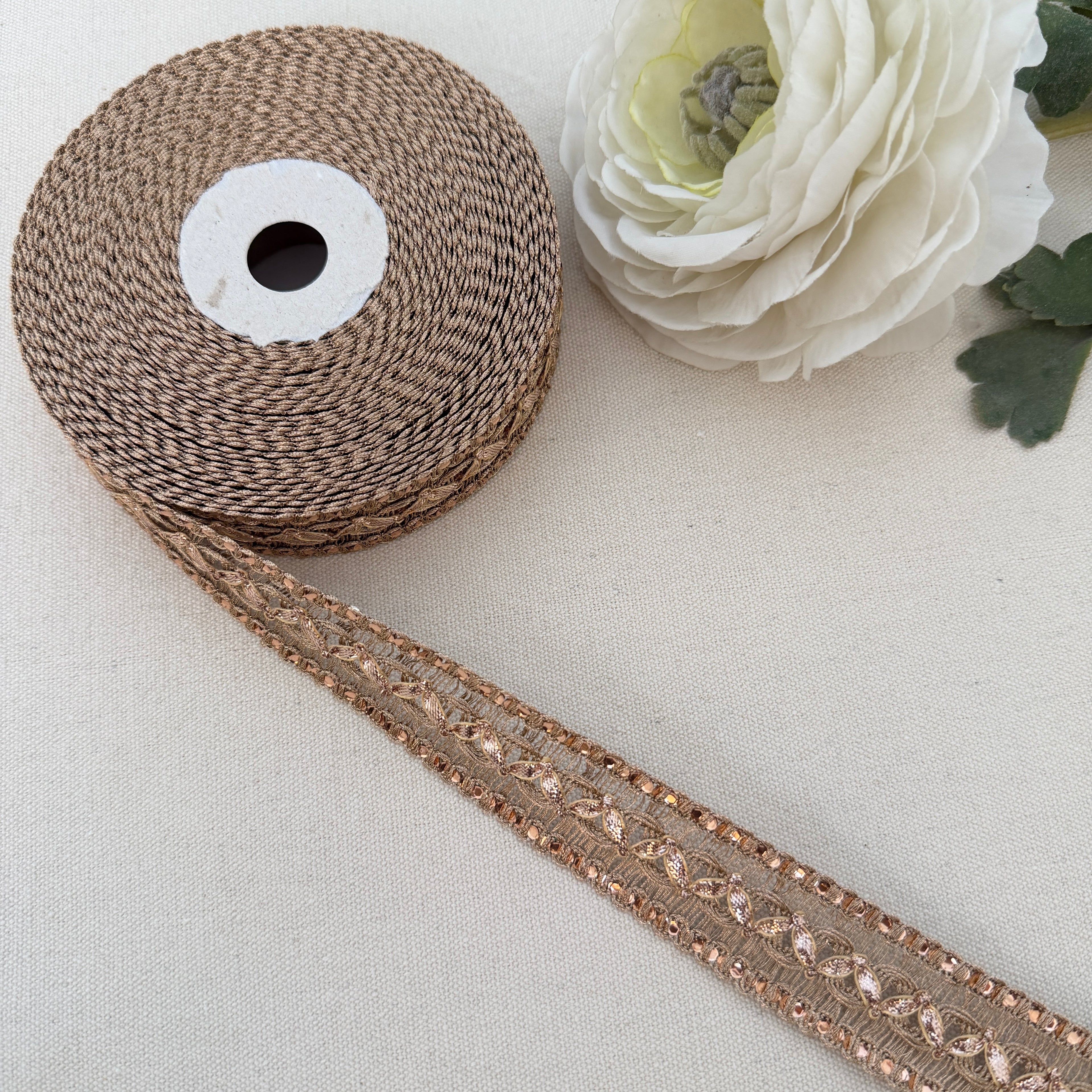 Spool of brown ribbon with decorative trim on a light background with a white flower.