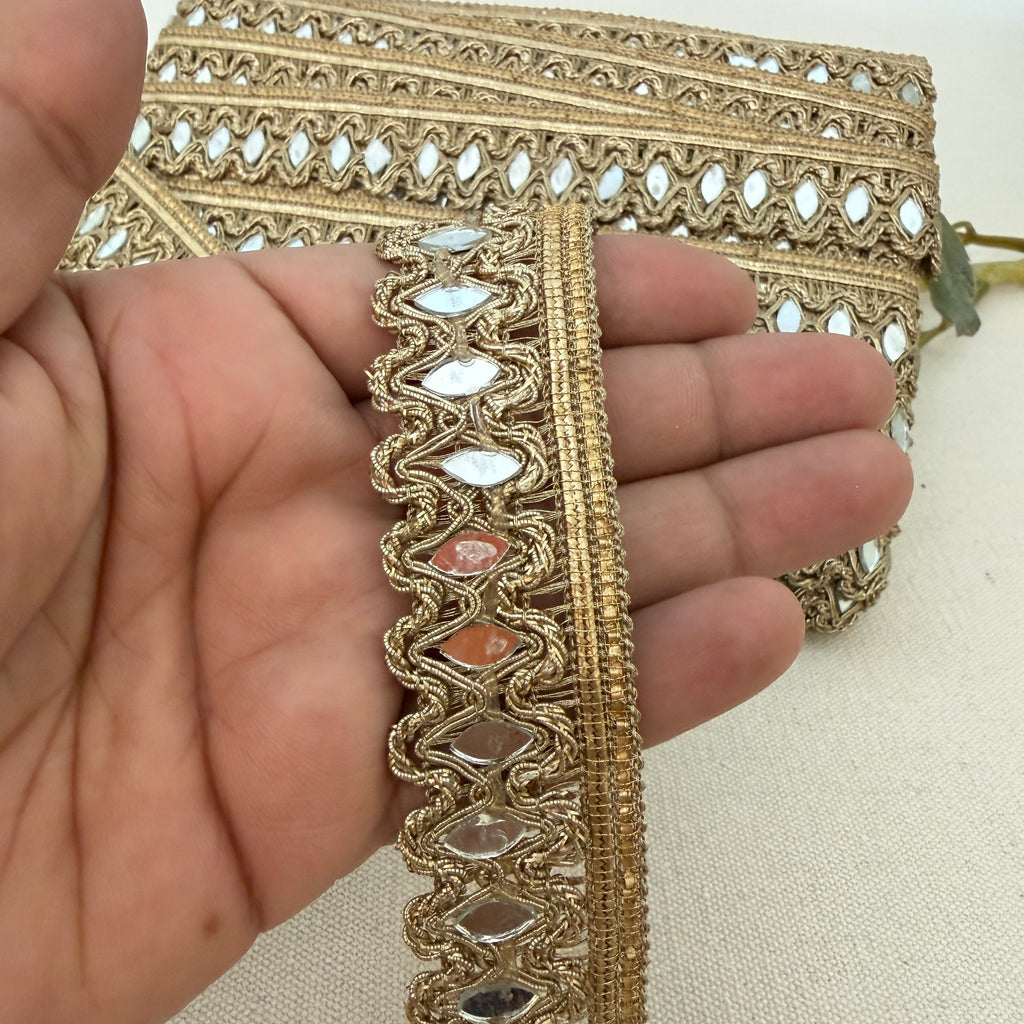Decorative gold fabric trim held between fingers on a neutral background