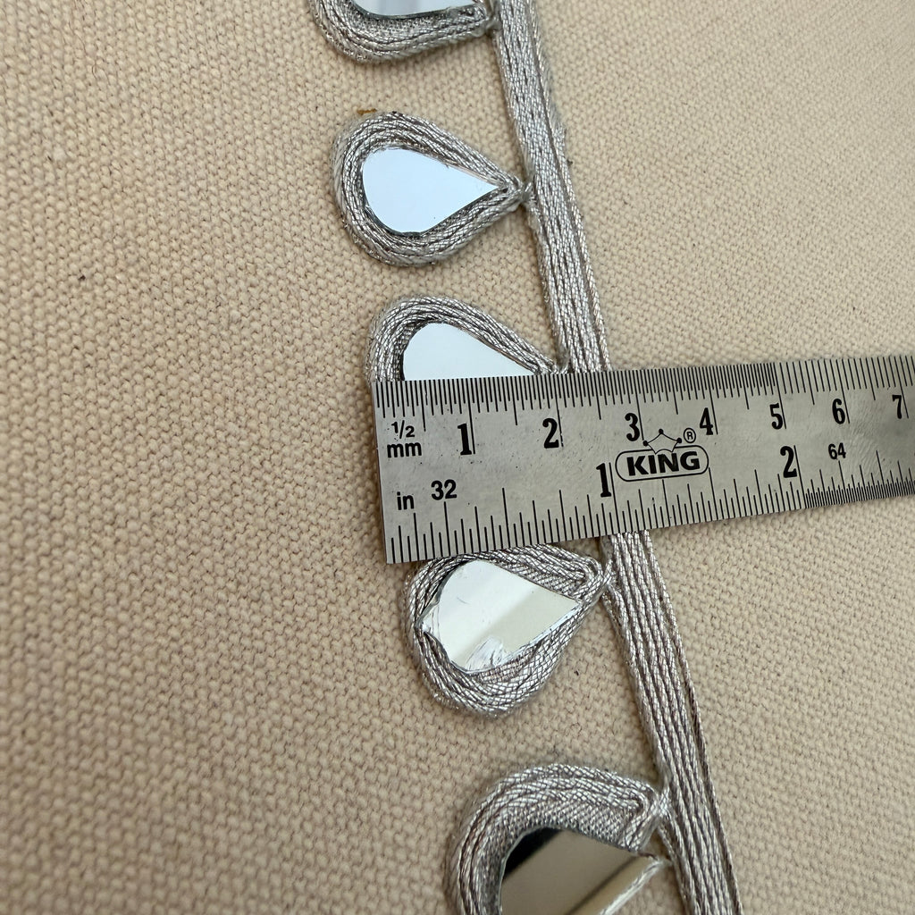 Decorative trim with teardrop shapes on a beige fabric background, measured with a ruler.