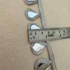 Decorative trim with teardrop shapes on a beige fabric background, measured with a ruler.