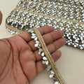 Close-up of a hand holding a decorative fabric strip with gold and silver embellishments.