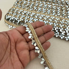 Close-up of a hand holding a decorative fabric strip with gold and silver embellishments.