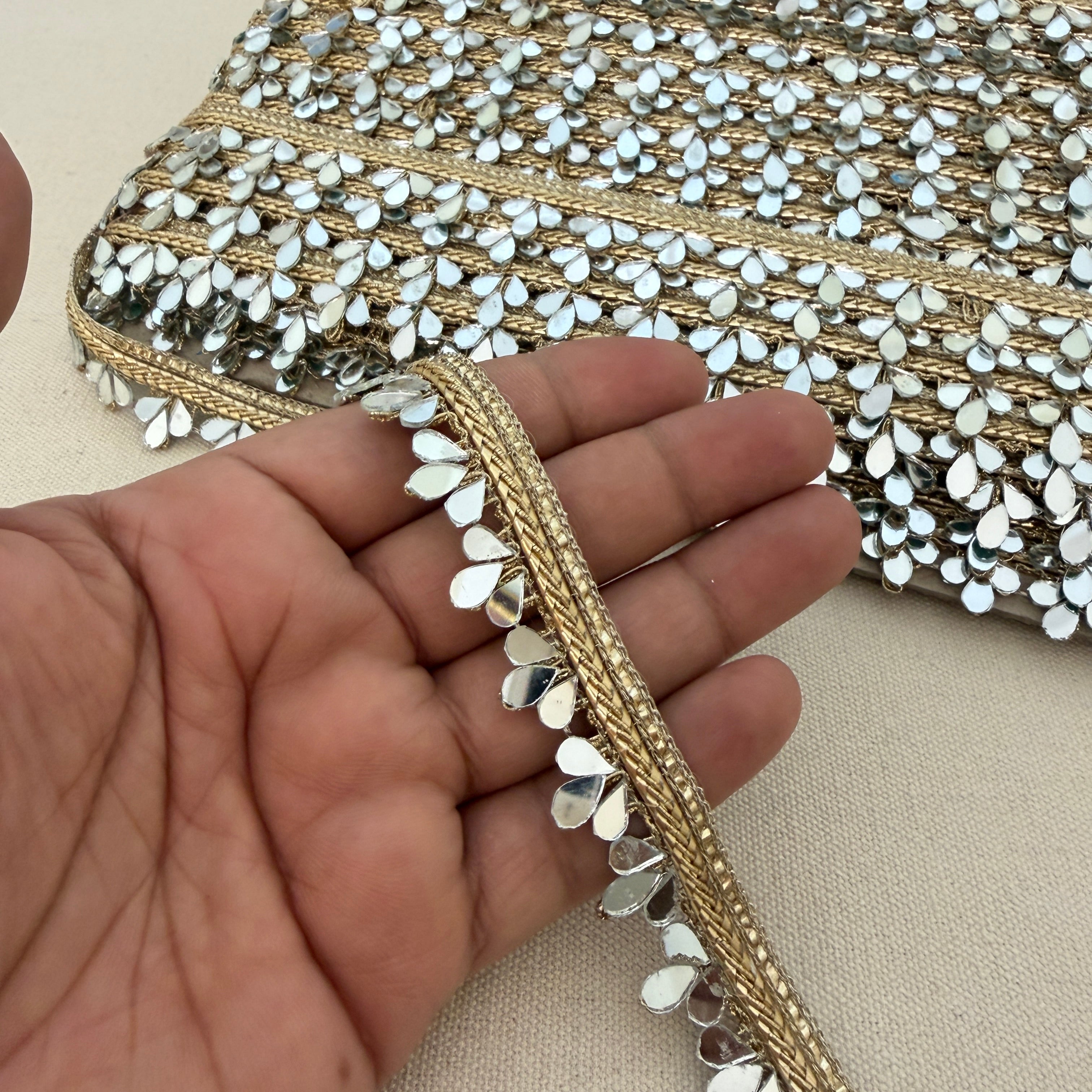 Close-up of a hand holding a decorative fabric strip with gold and silver embellishments.