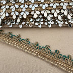 Close-up of decorative fabric trim with gold and silver details on a beige background