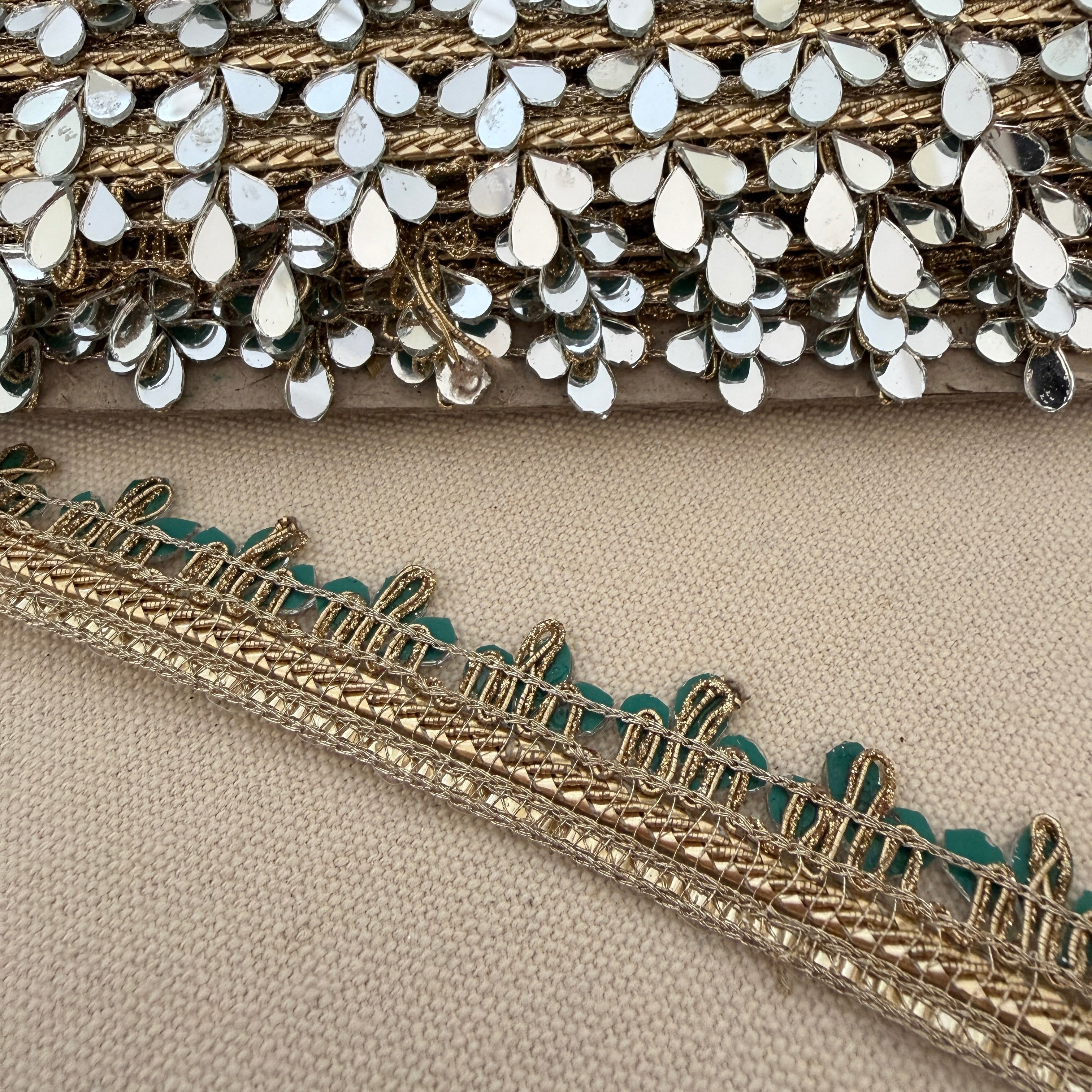 Close-up of decorative fabric trim with gold and silver details on a beige background