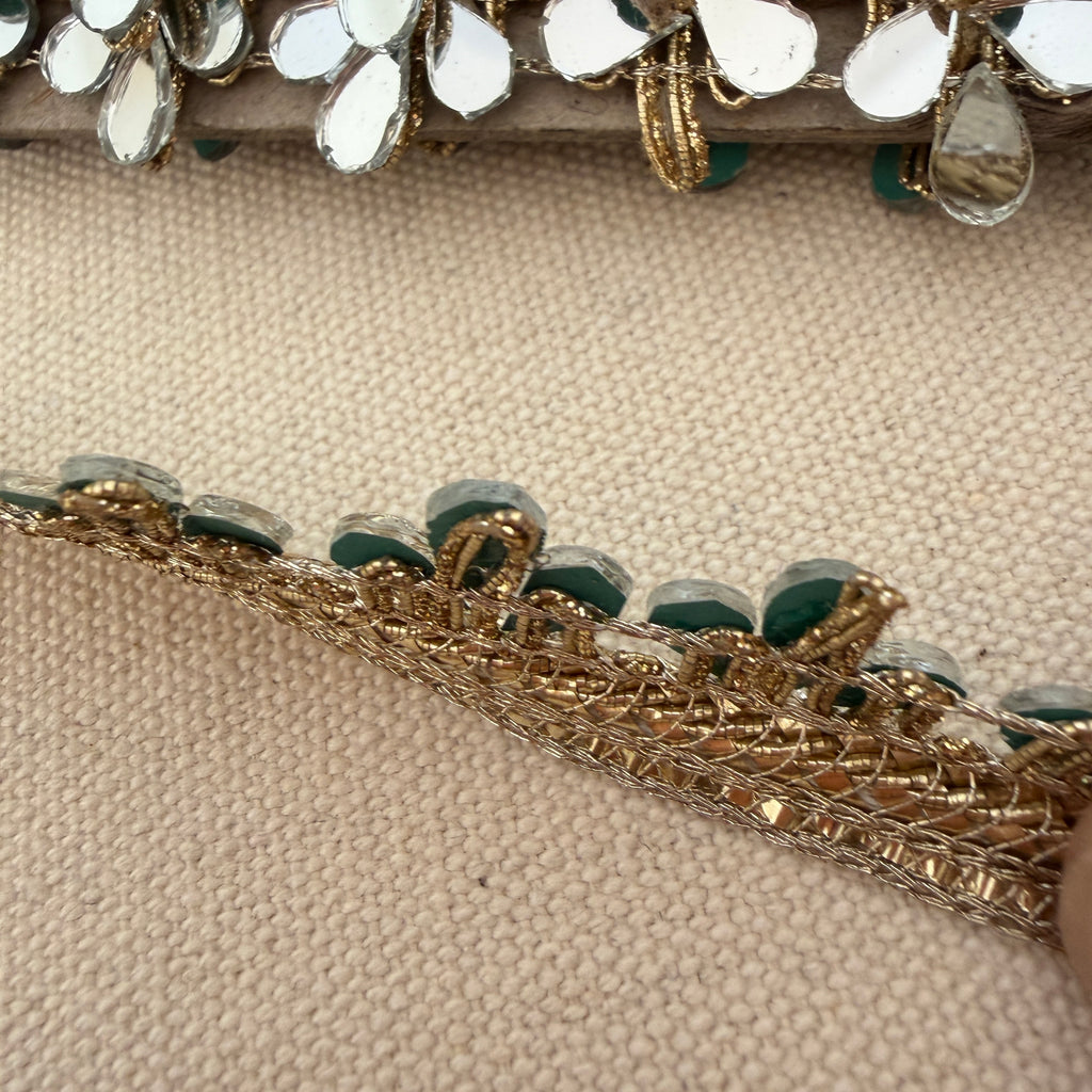 Close-up of decorative headband with gold and green embellishments on a beige fabric background