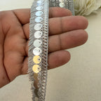 Silver sequin trim held between fingers on a neutral background
