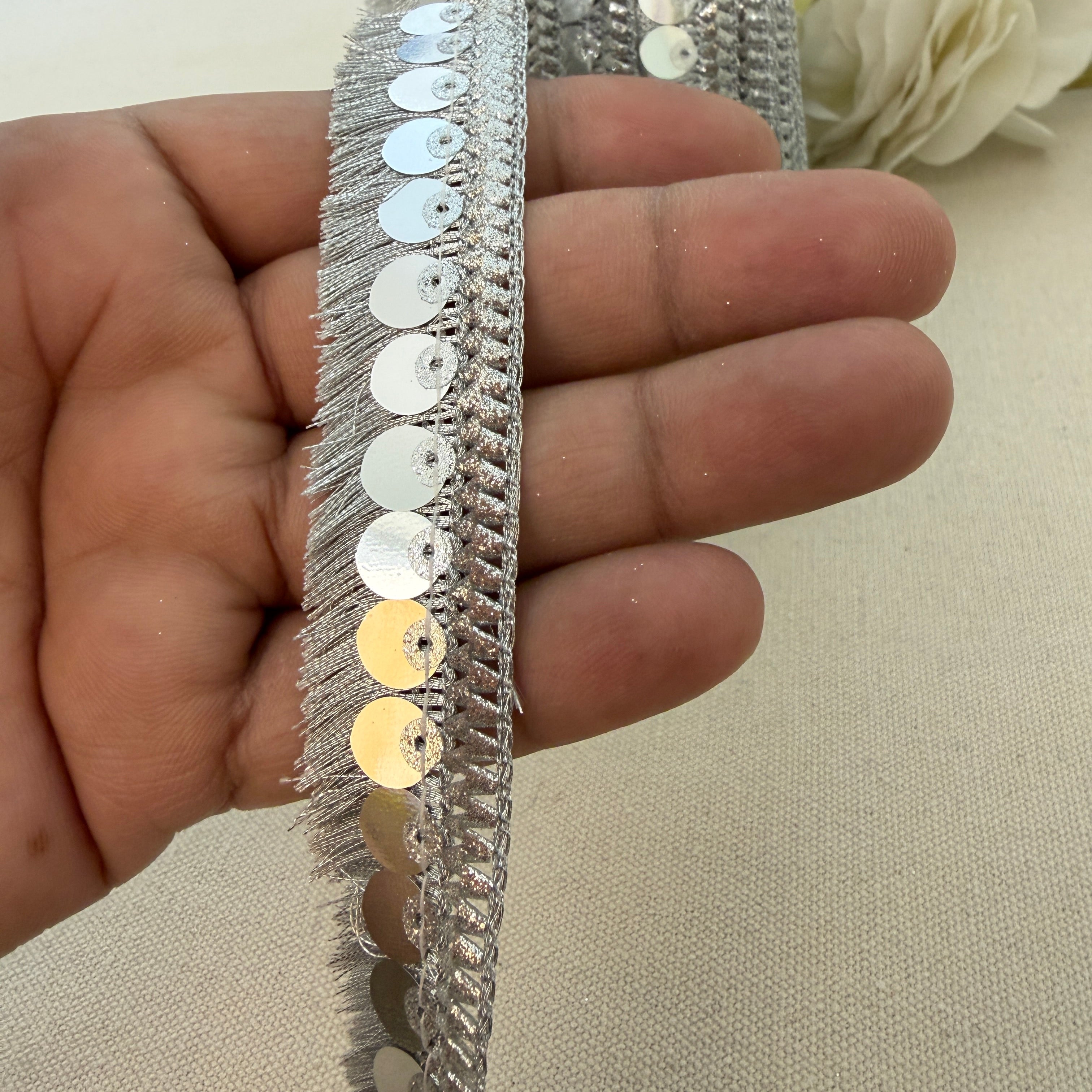 Silver sequin trim held between fingers on a neutral background