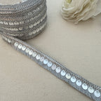 Silver sequin ribbon on a beige surface with a white flower.