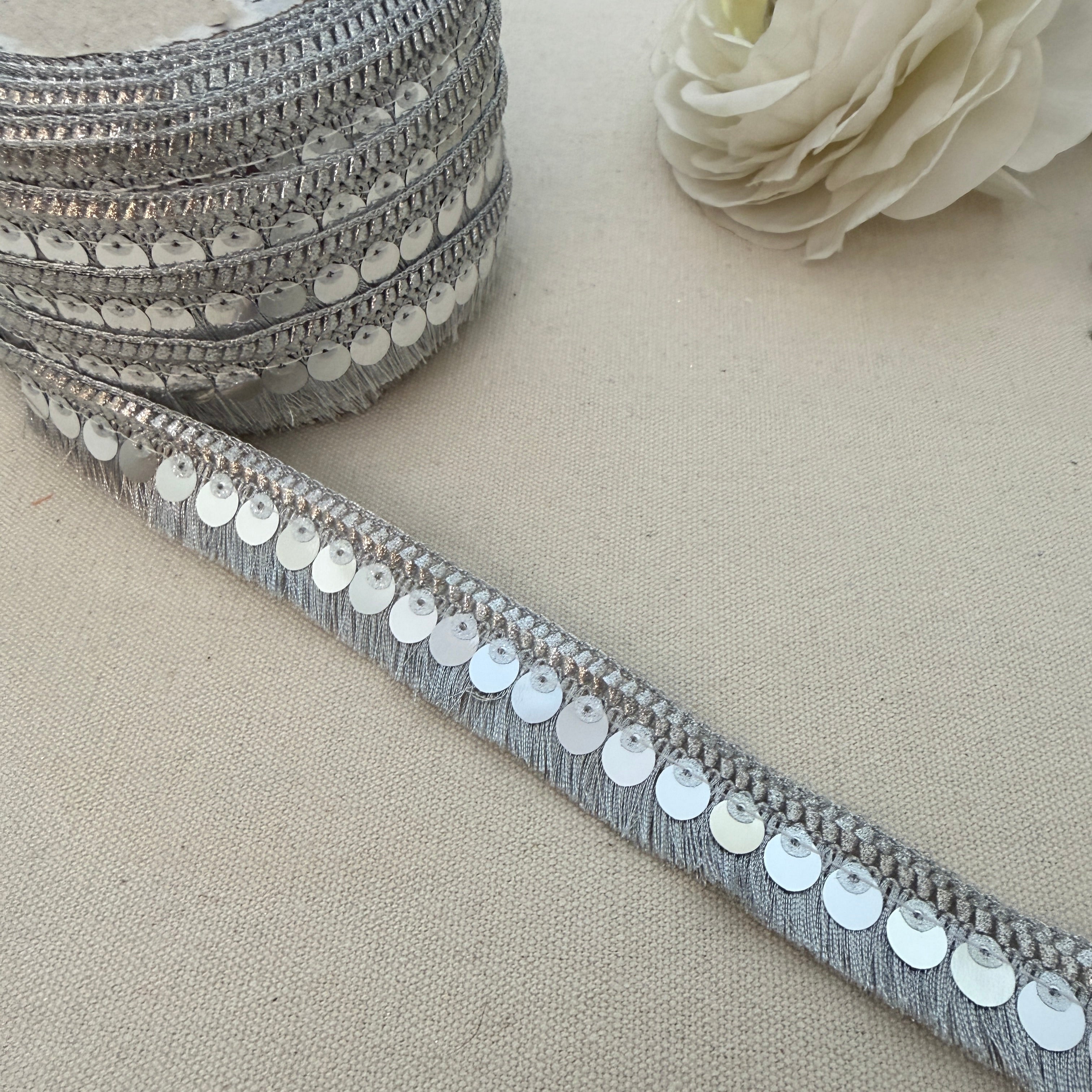 Silver sequin ribbon on a beige surface with a white flower.