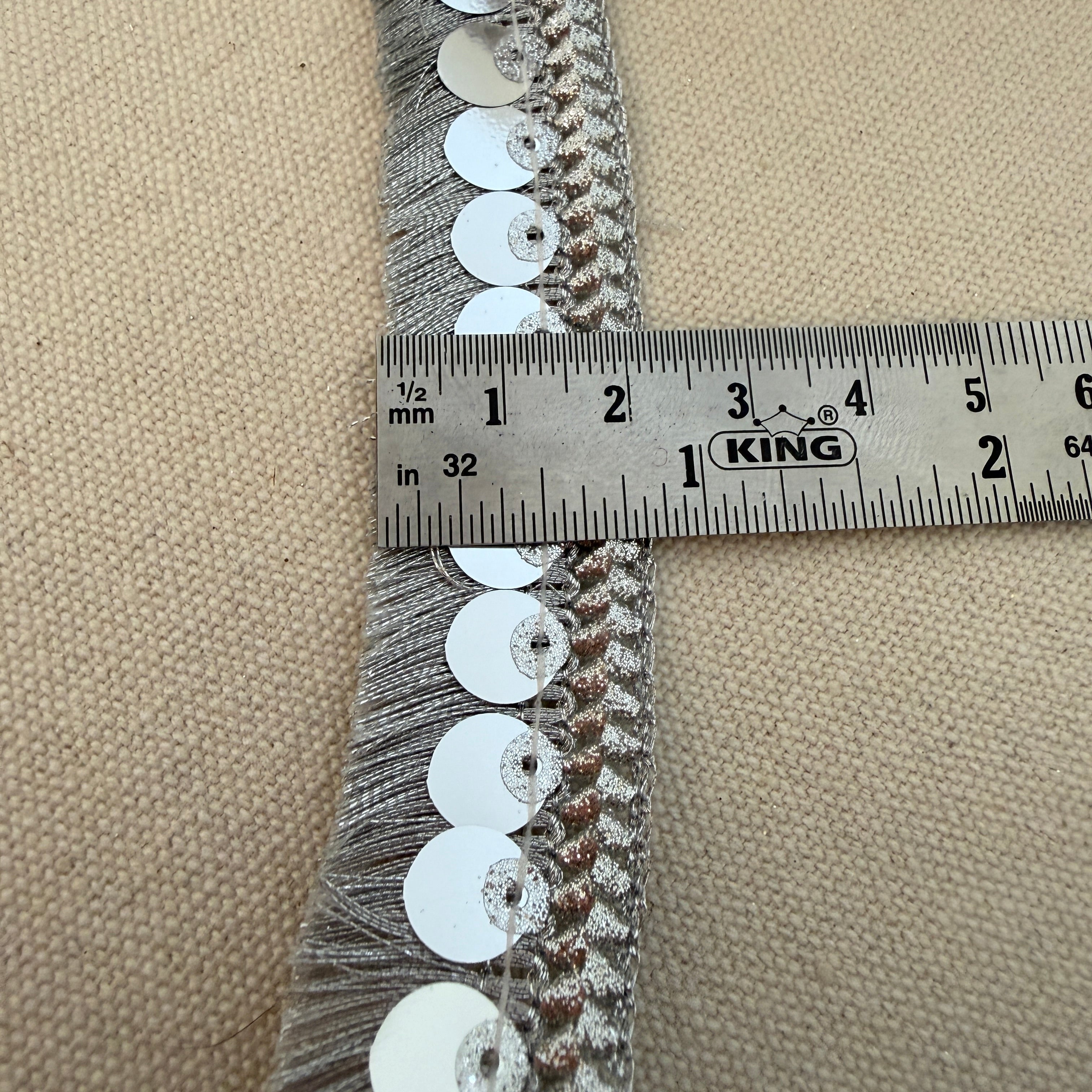 Sequined trim with a ruler for scale on a beige background